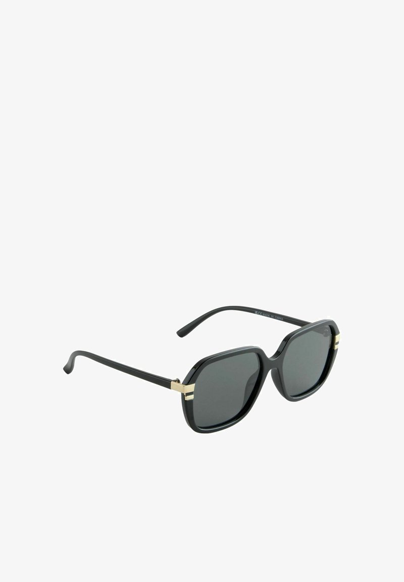 Lunettes de soleil noires surdimensionnées avec des verres foncés, de forme angulaire, et des accents en métal doré sur la monture. Branches en plastique avec une finition brillante.