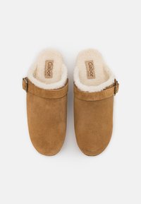 Braune Wildleder-Clogs mit Kunstfellfutter, ausgestattet mit einem seitlichen Riemen mit Schnalle. Flache Sohle und runde Zehenform. Einfache und gemütliche Optik.