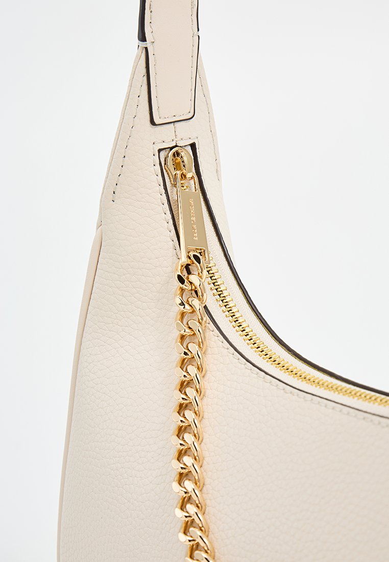 Sac à main en cuir crème avec une texture lisse, accent en chaîne dorée, fermeture zippée sur le dessus, et surpiqûres noires contrastantes le long des bords.