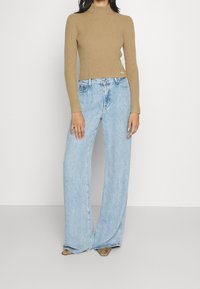 Suéter de cuello alto acanalado color canela combinado con unos vaqueros de pierna ancha en azul claro. Detalle destacado en dorado metálico en el suéter; tela texturizada en toda la prenda.