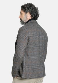 Blazer a cuadros grises con tejido texturizado, con un collar negro y acentos marrones. Corte entallado con puños abotonados y bolsillos laterales.