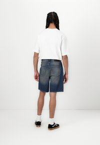 Denimshorts i en falmet blånyanse med rett snitt, kombinert med en hvit t-skjorte med korte ermer og svarte sneakers med hvite detaljer.