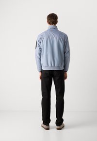 Light blue nylon jacket with high collar, elastic cuffs, and black accents; paired with black pants and beige shoes. Rear view.