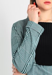 Rutig blazer med en design i teal och svart, med en skräddarsydd passform, vida ärmar och en ribbad svart topp under.