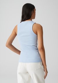 Top a canotta a coste blu chiaro con silhouette aderente, spalline larghe e scollatura rotonda. Abbinata a pantaloni bianchi a vita alta.