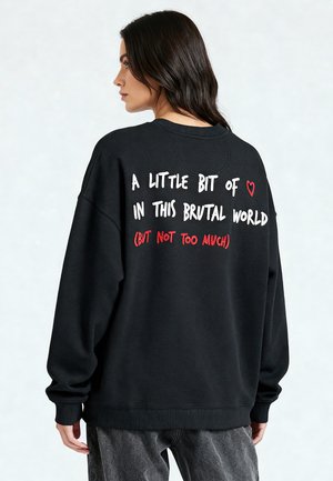 Pulover supradimensionat negru, cu text alb și roșu pe spate, având guler rotund și manșete dantelate, fabricat dintr-un material moale.