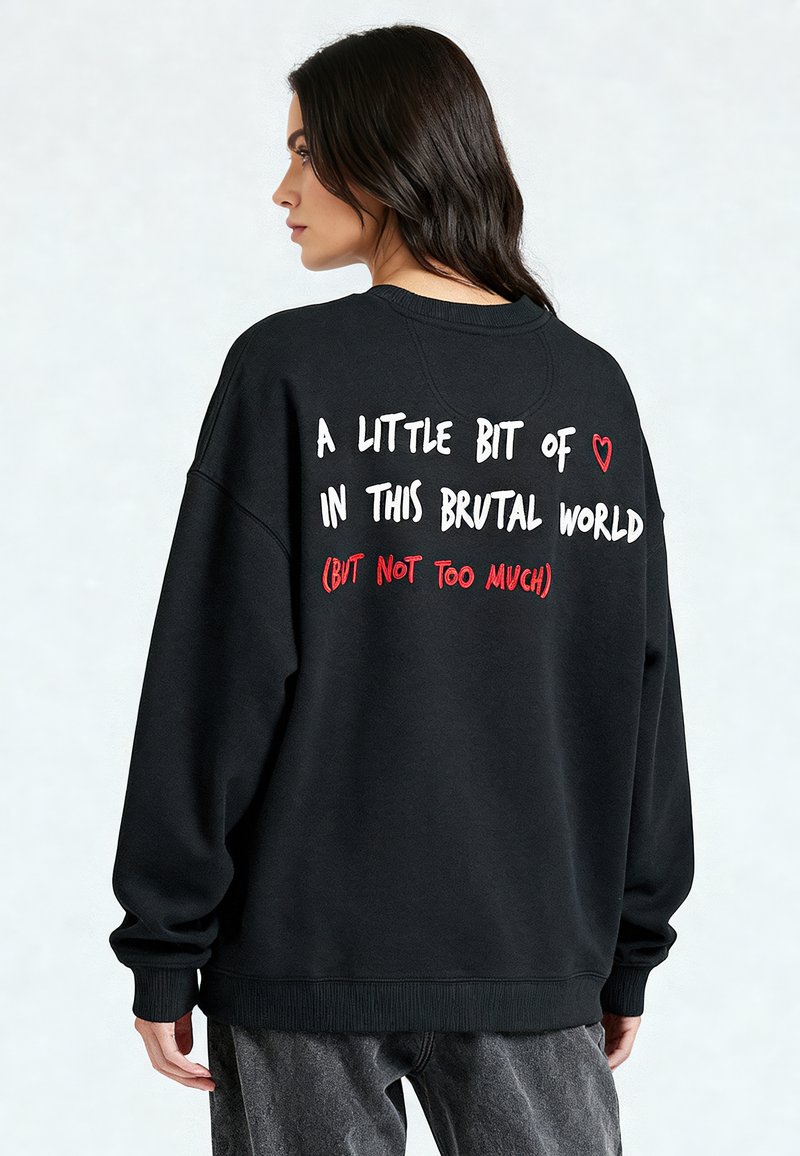 Fekete, oversized kapucnis pulóver, fehér és piros felirattal a háton, kerek nyakú és bordás mandzsettákkal, puha anyagból készült.