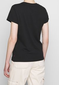 Camiseta de algodón negra con mangas cortas, cuello redondo clásico y un pequeño logo en el dobladillo. Presenta un corte holgado y una textura suave.