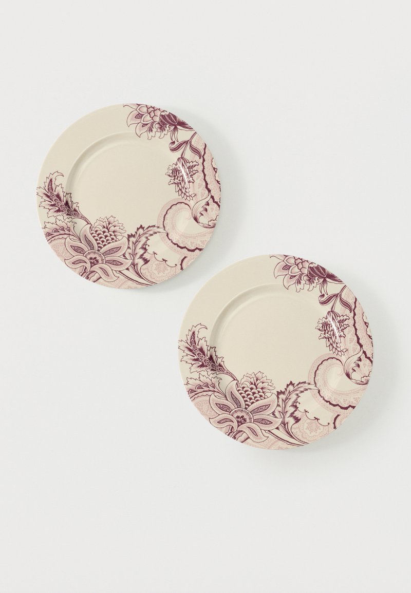 Deux assiettes en céramique beige avec des motifs floraux bordeaux ornementaux le long des bords sur un fond blanc uni.