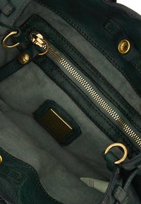 L'interno della borsa a tracolla verde in pelle presenta una zip dorata, hardware in ottone e una fodera in tessuto con una sottile trama. Include un'etichetta con il marchio.