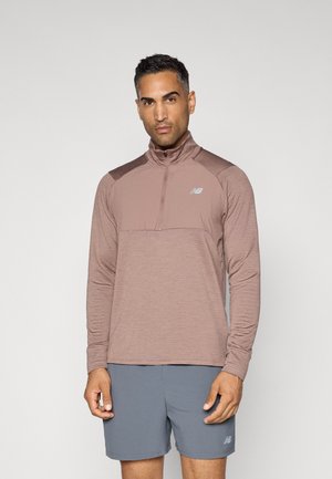Sportliches Langarm-Zip-Up-Oberteil in Hellbraun mit strukturiertem Stoff, kontrastierenden dunkelbraunen Schultern und einem kleinen Logo auf der Brust.