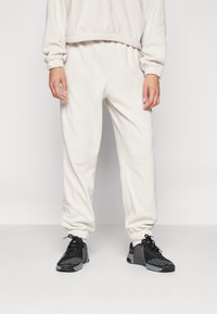 Pantalones jogger de forro polar color crema con puños y cintura elásticos, acompañados de zapatillas deportivas negras con un diseño texturizado.