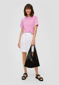 Roze katoenen t-shirt, witte linnen shorts, zwarte gevlochten handtas en zwarte sandalen met banden; in het algemeen een casual zomeroutfit.