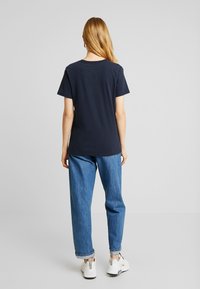 Mörkblå bomullst-shirt med korta ärmar och rund halsringning. Kombinerad med ljusblå jeans och vita sneakers. Enkel design utan synliga mönster.