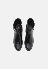 Paire de bottines en cuir noir avec fermeture éclair latérale et bouts arrondis, vues de dessus sur un fond blanc.