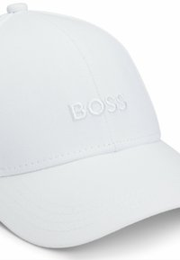 Fehér baseball sapka texturált anyagból, a fronton hímzett "BOSS" logóval, öltött karimával és állítható hátsó pánttal.