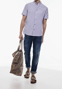 Jasnofioletowa, krótko rękawowa koszula zapinana na guziki z kołnierzykiem typu band, połączona z niebieskimi dżinsami i brązowymi sandałami. Osoba trzyma beżową torbę.