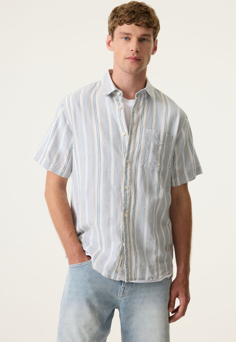 Short-sleeve button-up shirt in light blue and white vertical stripes, made of textured fabric with a patch pocket and curved hem.