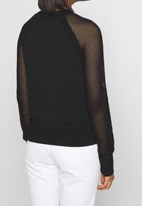 Czarny sweter z gładkim korpusem i długimi rękawami z siateczki w czołowej części. Ribbed mankiety i dół, prezentujące nowoczesny design.