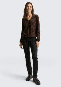 Bruine luipaardprint blouse met lange mouwen, een v-hals en een geraffineerde detail aan de voorkant, gecombineerd met zwarte slim-fit broek en chunky zwarte schoenen.