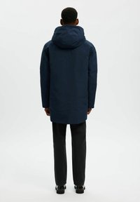 Parka impermeabile blu navy con cappuccio, caratterizzata da un taglio dritto e un design minimalista. La vista posteriore mostra una texture liscia e nessuna ferramenta visibile.