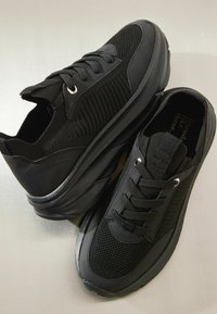 Melnas sporta kurpes no acs un sintētiskām materiāliem. Tām ir apaļas zolītes, auklas un papēža cilpa ērtai uzvelkšanai.