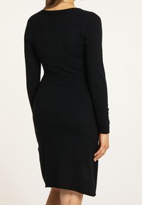 Robe noire à manches longues avec une silhouette ajustée, une texture lisse et des accents côtelés le long de la taille et des poignets.