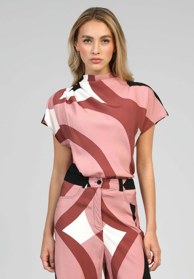 Top à manches courtes avec un motif abstrait rose, rouge et blanc, doté d'un col montant ; associé à un pantalon avec accents noirs présentant des designs géométriques.