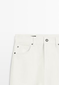 Białe jeansy z denimu z talią o średnim stanie, metalowymi elementami i dwoma przednimi kieszeniami. Charakteryzują się gładką teksturą i starannym przeszyciem.