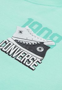 Mintgrønn hettegenser med grafikk av svart-hvite Converse-sko og teksten "1000 CONVERSE" i fet, kontrasterende farger.