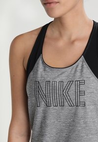 Canotta grigia in heather con accenti neri, caratterizzata dal logo "NIKE" in bold nero sul petto, realizzata in un tessuto leggero.