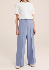 Vit kortärmad blus med ett strukturerat zickzackmönster och rund halsringning, paired med högmidjade, vida ljusblå byxor.