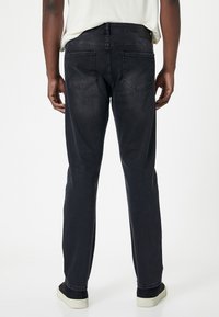 Mörka denimjeans med rak passform, synlig sömnad och två bakfickor. Matchade med svarta skor och en ljusfärgad skjorta.
