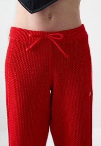 Punaiset verkkokudot juoksuhousut sisältävät joustavan vyötärönauhan ja kiristysnarun, sivutaskut sekä kevyen ja hengittävän kankaan.