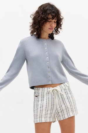 Light blue cropped cardigan with a round neckline, button closure, and ribbed cuffs, paired with white striped shorts featuring a drawstring.