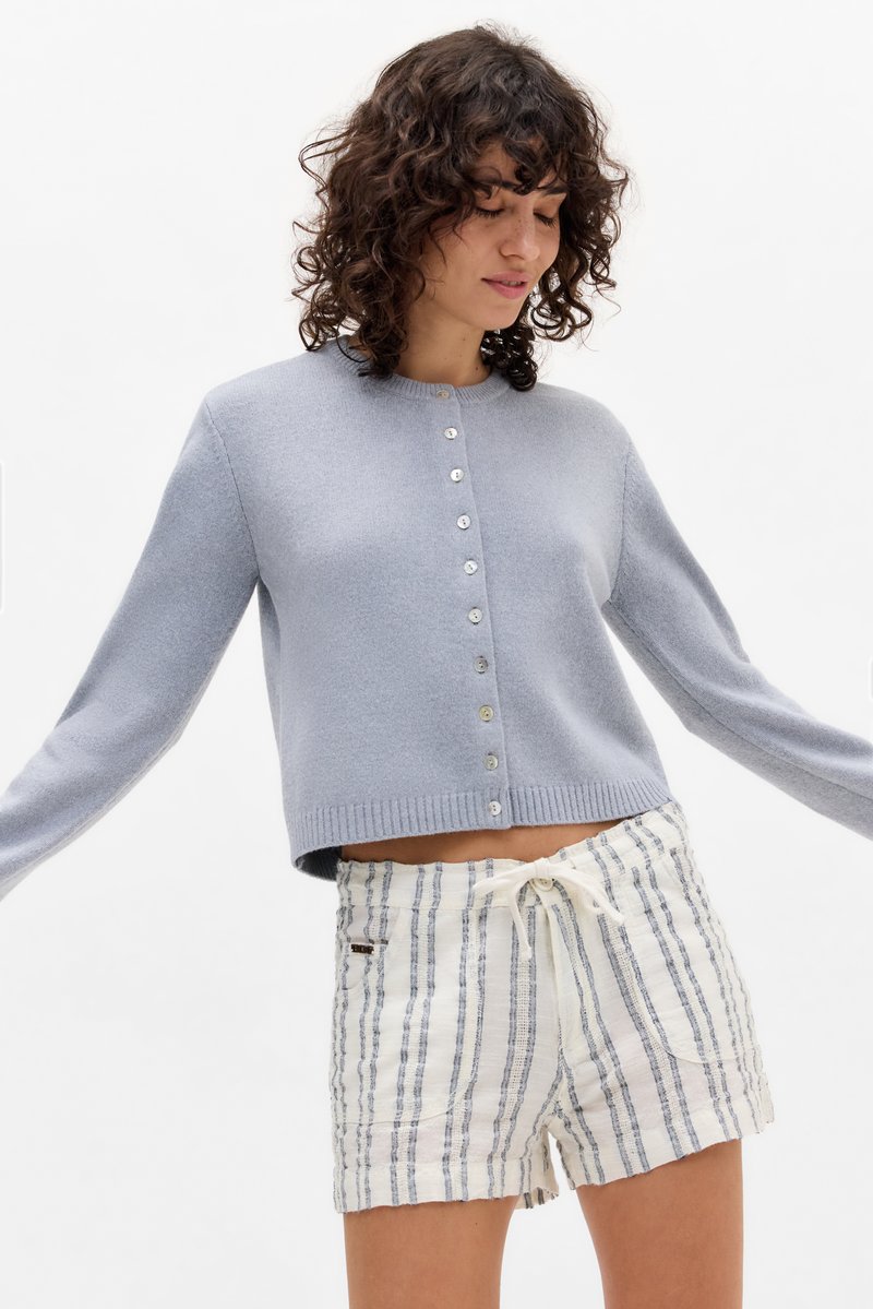 Light blue cropped cardigan with a round neckline, button closure, and ribbed cuffs, paired with white striped shorts featuring a drawstring.