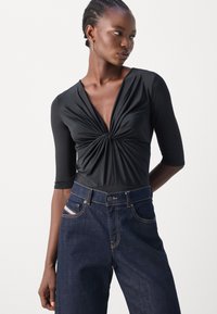 Svart langermet body med dyp V-hals og vridd frontdesign, sammen med mørkeblå høyt midjet jeans med synlige sømdetaljer.