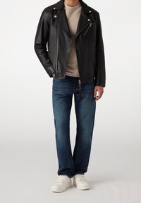 Schwarze Lederbikerjacke mit silberner Hardware, beiger Rundhalsausschnitt-Shirt, blaue Jeans und weiße Sneakers. Lässige Outfit-Kombination.