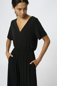 Svart jumpsuit med V-ringning, korta ärmar och elastisk midja. Har sidofickor och en slät yta.