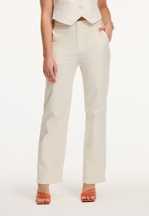Pantalons beiges taille haute en tissu lisse, avec une coupe droite et une fermeture éclair. Associés à des sandales à talons hauts orange à lanières.