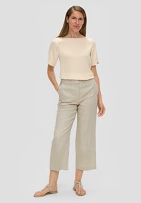 Beige top met korte mouwen en vierkante halslijn, gecombineerd met lichtgrijze, wijdvallende broek en beige sandalen met banden.