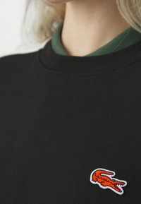 Felpa nera con colletto rotondo, caratterizzata da un grande logo di coccodrillo ricamato arancione sulla parte sinistra del petto.