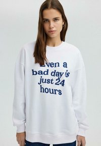 Witte sweatshirt met marineblauwe tekst "Zelfs een slechte dag is slechts 24 uur." Heeft een ronde halslijn en gefronste mouwen. Casual pasvorm.