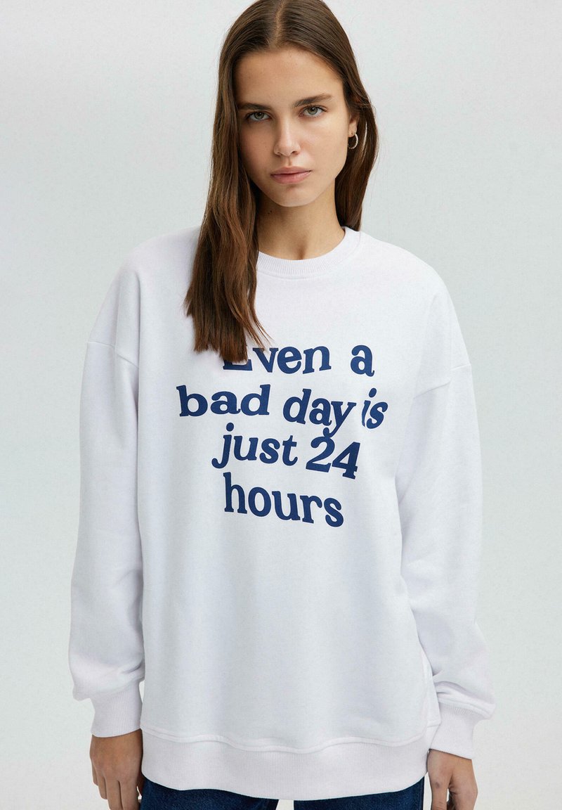 Witte sweatshirt met marineblauwe tekst "Zelfs een slechte dag is slechts 24 uur." Heeft een ronde halslijn en gefronste mouwen. Casual pasvorm.