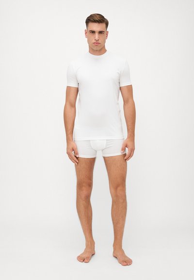 Weißes kurzärmliges Hemd aus glattem Stoff, kombiniert mit weißen, taillierten Shorts. Beide Kleidungsstücke zeichnen sich durch ein minimales Design und dezenten Besatz aus.