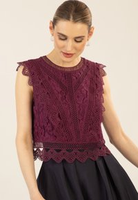 Burgunderfarbenes Spitzenoberteil mit gewellten Kanten und komplexen Mustern; enganliegendes Design mit einem strukturierten Oberteil über einem glatten dunklen Rock.