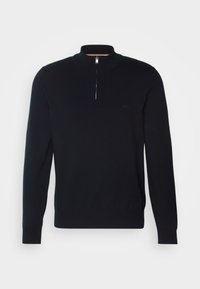 Svart stickad tröja med hög krage och halv dragkedja. Har subtil varumärkeslogotyp på bröstet samt ribbade ärmslut och fåll.