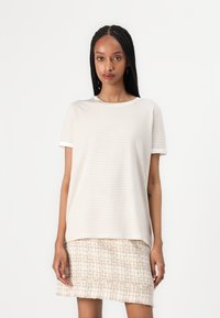 Camiseta de manga corta a rayas color crema, hecha de una tela suave, combinada con una falda clara texturizada y con flecos. Cuello redondo sencillo.