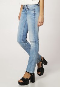 Jeans skinny azul claro con un acabado desgastado, diseño de cinco bolsillos y cintura de altura media, combinados con sandalias de plataforma negras.