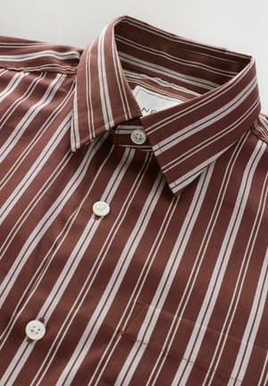 Brązowa koszula z pionowymi białymi paskami, z klasycznym kołnierzykiem i dwoma białymi guzikami. Gładki materiał z detalem kieszeni.